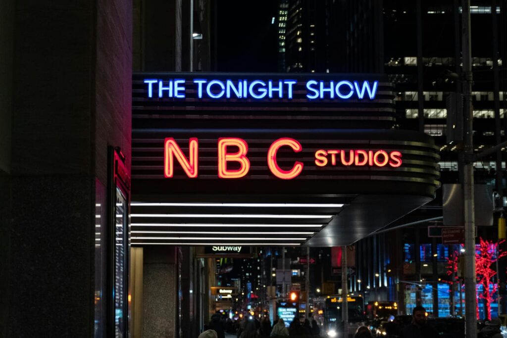 NBC Studios at night in New York with The tonight Show sign showing NBC News headquarters and its influence on US media, finance, and stock market trends 